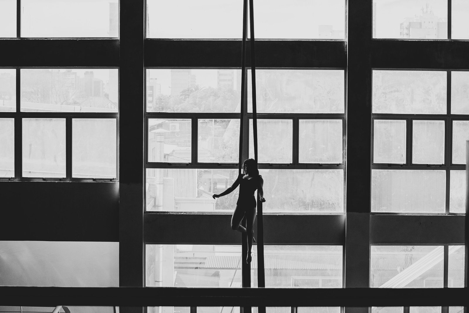 Aerial gymnast silhouetted against large windows in a Buenos Aires building.