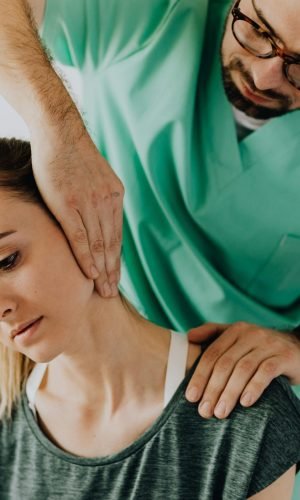 Confident doctor wearing uniform and eyeglasses gently doing therapeutic massage on calm female patients neck and stretching stiff neck muscles